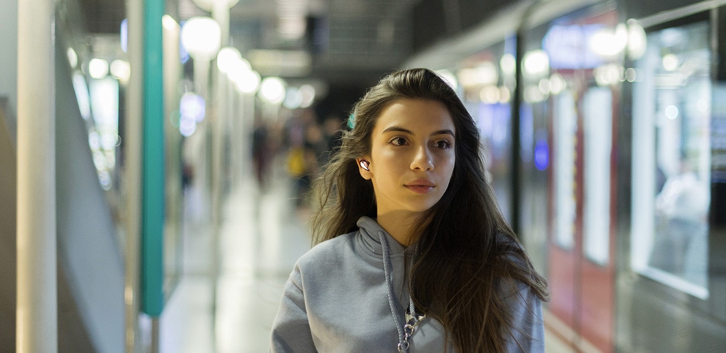 A woman wearing a Buds Live is walking in a subway station. Below is a sound wave with an ANC OFF button selected on the very bottom to indicate that the noise cancelling mode is off.