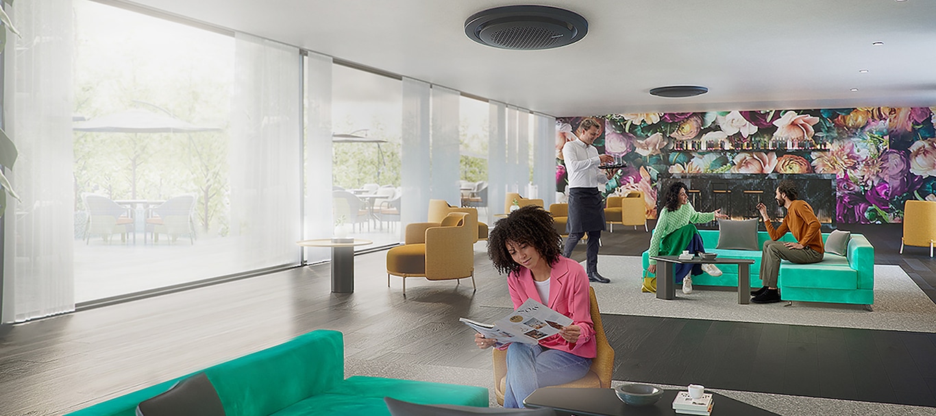 Two Samsung 360 cassette air conditioners are mounted on the ceiling of a sunlit lounge. Under one air conditioner, a woman reads a newspaper, while beneath the other, two people engage in conversation on a sofa and a man in a half apron serves glasses of water. 