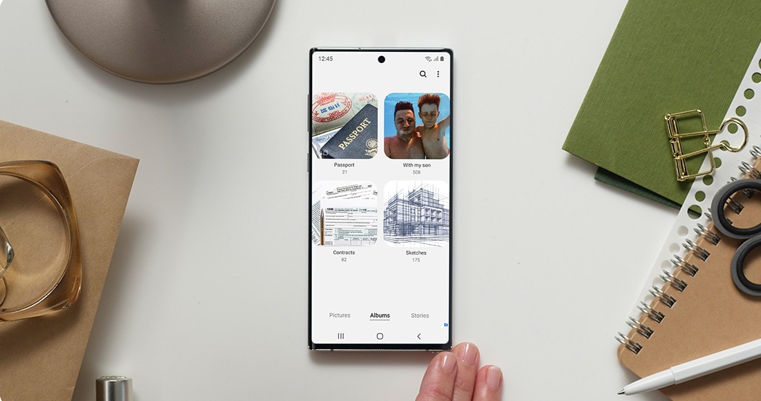 +Galaxy Note10 موضوع على جانبه الخلفي أعلى سطح المكتب، ومعروض على شاشته واجهة Secure Folder التي تعرض تطبيق Gallery (المعرض) المشتمل على ألبومات هي Passport (جواز السفر) وWith my son (مع ابني) وContracts (العقود) وSketches (الرسومات). وتبيِّن الصورة الكيفية التي يستطيع بها المستخدم الاحتفاظ ببيانات عمله الحساسة في أمان، إلى جانب محتوياته الشخصية