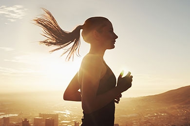Una mujer que corre con un amanecer de fondo. Su cabello se mueve con el viento para mostrar el movimiento dinámico.