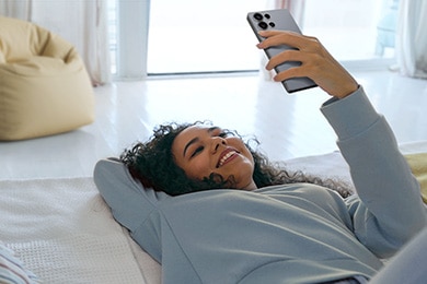 Una mujer está acostada en el piso sonriendo y mirando el Galaxy S25 Ultra con una bolsa de porotos amarillos visible detrás de ella.