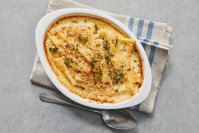 Los bastones de nabos cubiertos con salsa de parmesano gratinada y otros ingredientes están en un cuenco blanco.