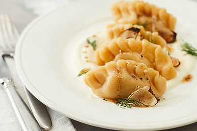 Dumplings al vapor rociados con manteca y condimentados con pimienta negra y ciboulette en un plato blanco.