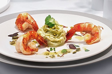 Presentación de tres langostinos a la sartén con ensalada de pepino en un plato blanco.
