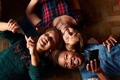 Tres niñas pequeñas recostadas boca arriba jugando con sus teléfonos inteligentes.