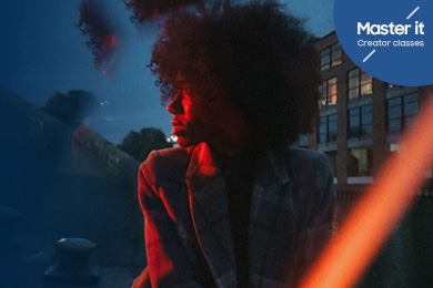 Una mujer con una chaqueta que mira hacia la izquierda, sutilmente iluminada por una luz roja frente a un cielo azul. Master it Creator classes