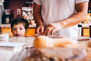 Child peers over counter while man preps food