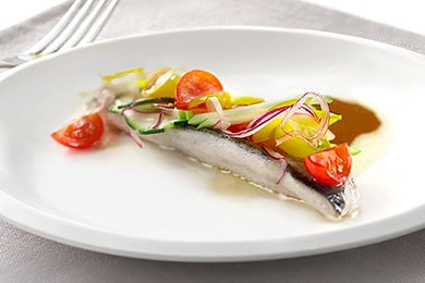 Un filete de trucha en un plato blanco decorado maravillosamente con verduras de colores encima.