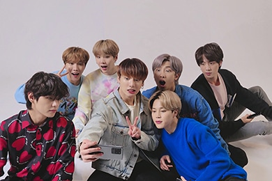 BTS se toma una selfie grupal. Todos los miembros están sentados en el suelo y tomándose una selfie de BTS con el Galaxy S20+ que está en poder de Jung Kook.