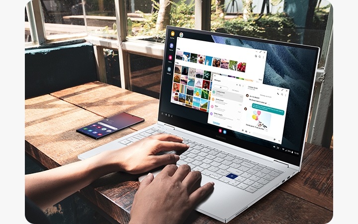 Использование ноутбука Samsung. Рядом с ноутбуком показан смартфон Galaxy с главным экраном на дисплее. С помощью приложения Dex пользователь просматривает на экране ноутбука фотоснимки из Галереи и одновременно отправляет текстовые сообщения.