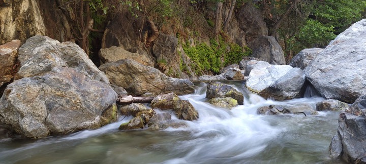 A scene of rushing water flowing over and around medium to large rocks in a river. The white water has been captured with long-exposure photography, giving it an ethereal, silky effect. 