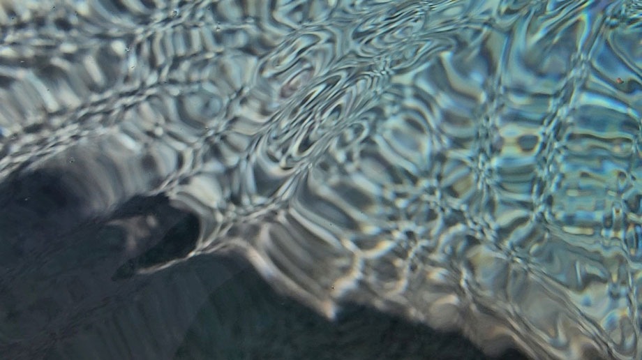 A close-up of water undulating and moving against the bottom of the water body, brightly lit by the sun.