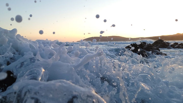 A close up of water crashing over some small rocks along a shore, shot right from the water level.