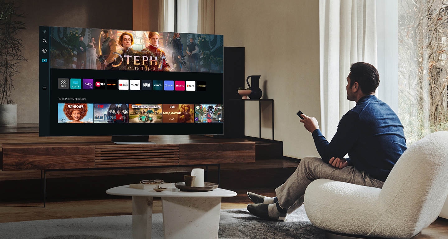 Мужчина с пультом в руке изучает новый пользовательский интерфейс Smart Hub на экране телевизора Samsung Neo QLED в гостиной