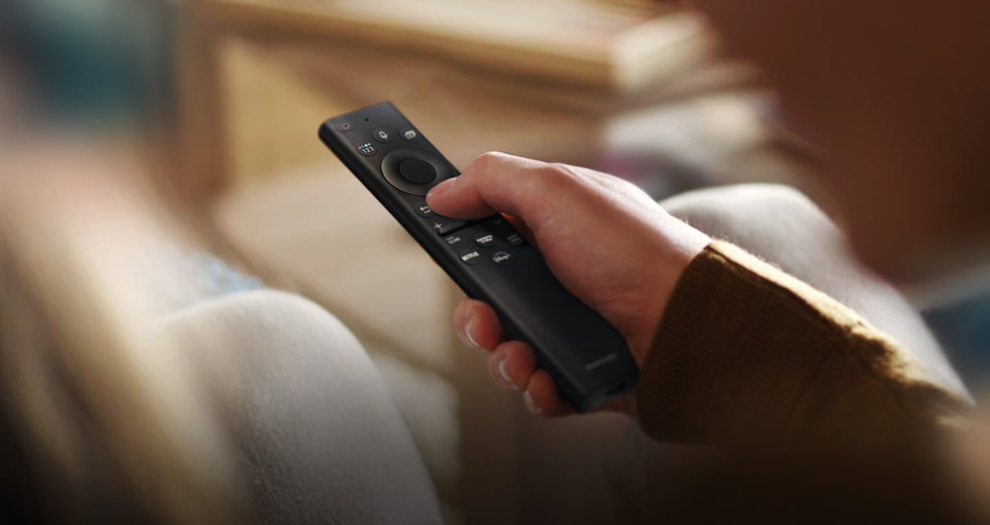 На дисплее крупным планом изображена рука, нажимающая на пульт One Remote.