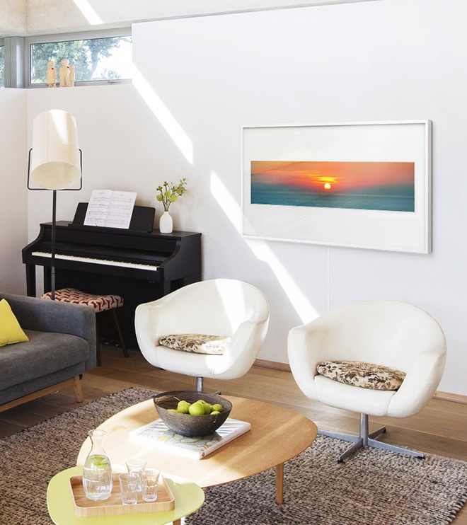 Рамка на стене с фотографией заката в панорамном макете с матовым цветом Polar White в гостиной с креслами. Рядом с Фреймом стоит пианино.