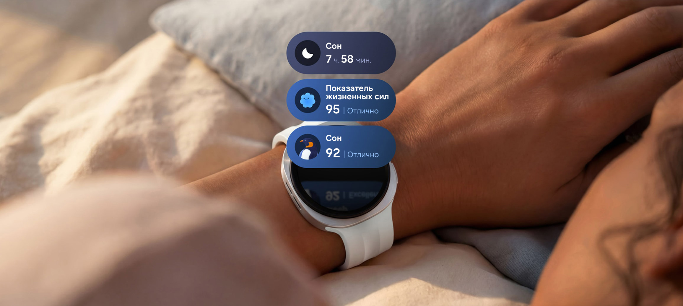 Galaxy Watch9 цвета белое золото со спортивным ремешком кремового надеты на запястье. Над дисплеем Galaxy Watch9 отображаются три информационных блока: данные о продолжительности сна (7 ч. 58 мин.), показатель жизненных сил Отлично (95 баллов) и блок с рекомендациям по сну с символом пингвина и показателем сна Отлично (92 балла).