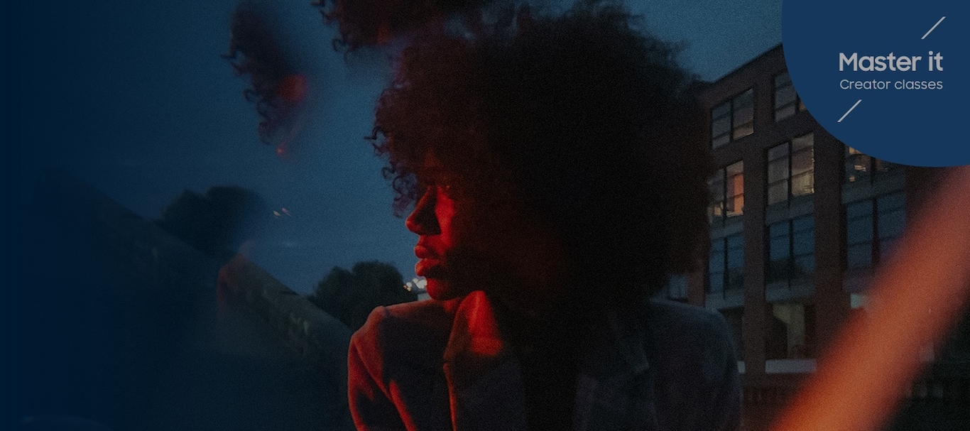 En kvinna i en jacka som tittar åt vänster, diskret upplyst av ett rött ljus framför en blå himmel. Master it Creator classes. Fotograferad #withGalaxy S22 Ultra1.