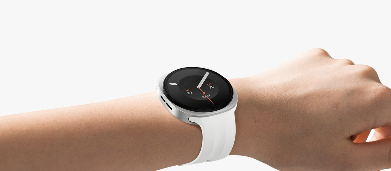 Galaxy Watch9 i Cream med Sport Band i Cream syns på en persons handled, lätt vinklad åt höger, som framhäver klockans slimmade och mjuka utseende med den karakteristiska cushion design, samt det tunna och flexibla Sport Band för en tajt och bekväm passform hela dagen med minimalt glapp tack vare Dynamic Lug System.