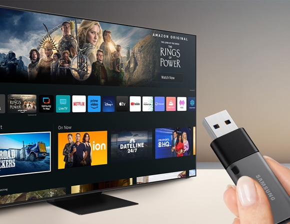 Person holding a USB flash drive next to a Samsung TV displaying the Home screen.