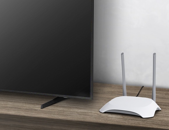 Router placed next to a Samsung Smart TV on a wooden table, highlighting the setup for a Wi-Fi connection.