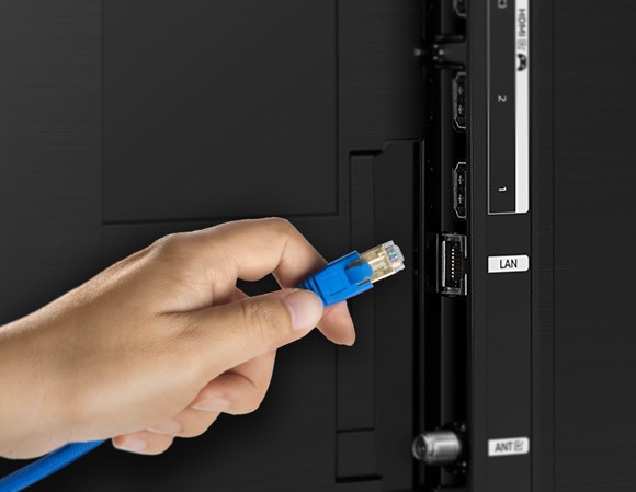 Close-up of a hand plugging a blue Ethernet cable into the LAN port on the back of a Samsung Smart TV.