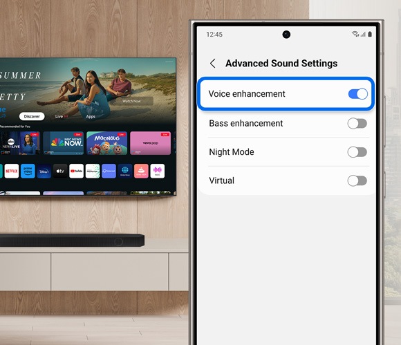 Phone screen displaying the Advanced Sound Settings in the SmartThings app, with the 'Voice enhancement' option toggled on, next to a Samsung Smart TV.