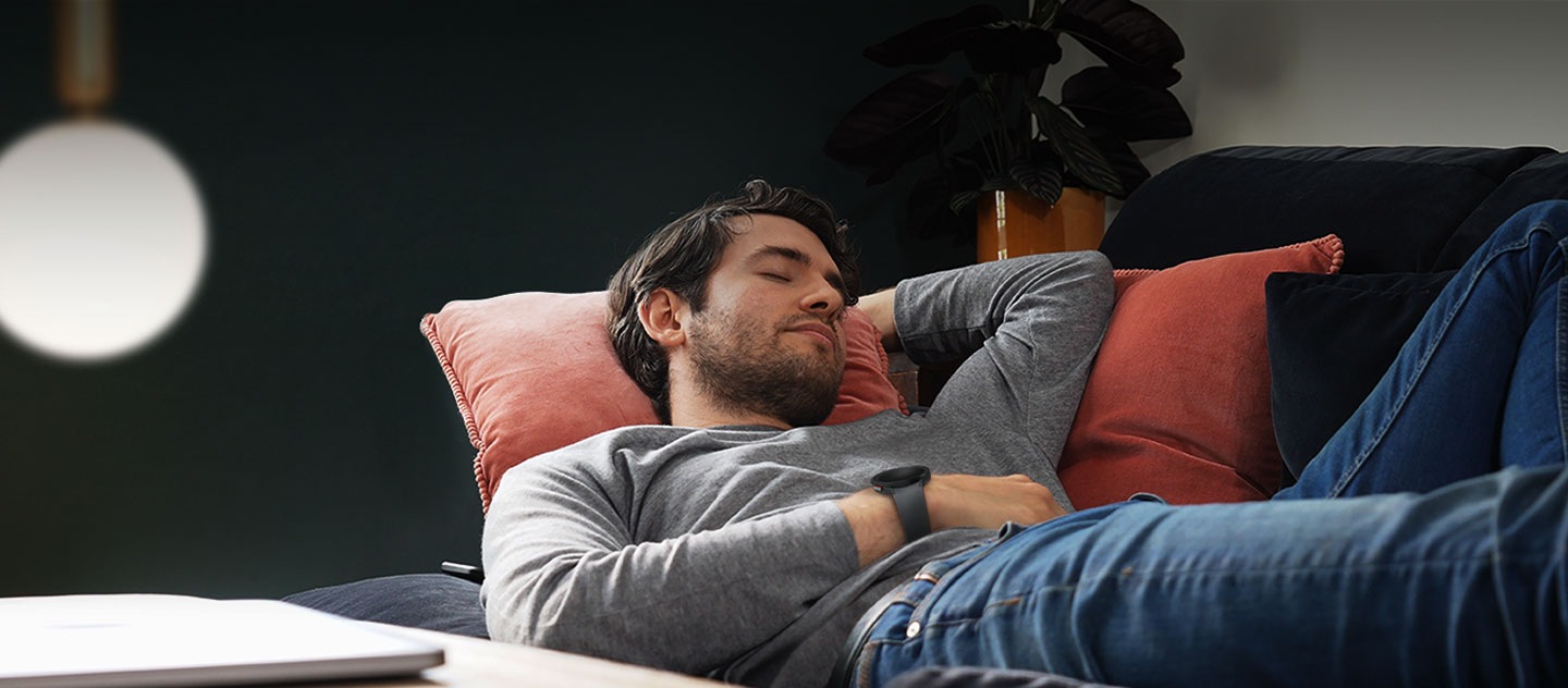 Бугуйндаа Galaxy Watch зүүсэн нэг эрэгтэй буйдан дээр унтаж байна.