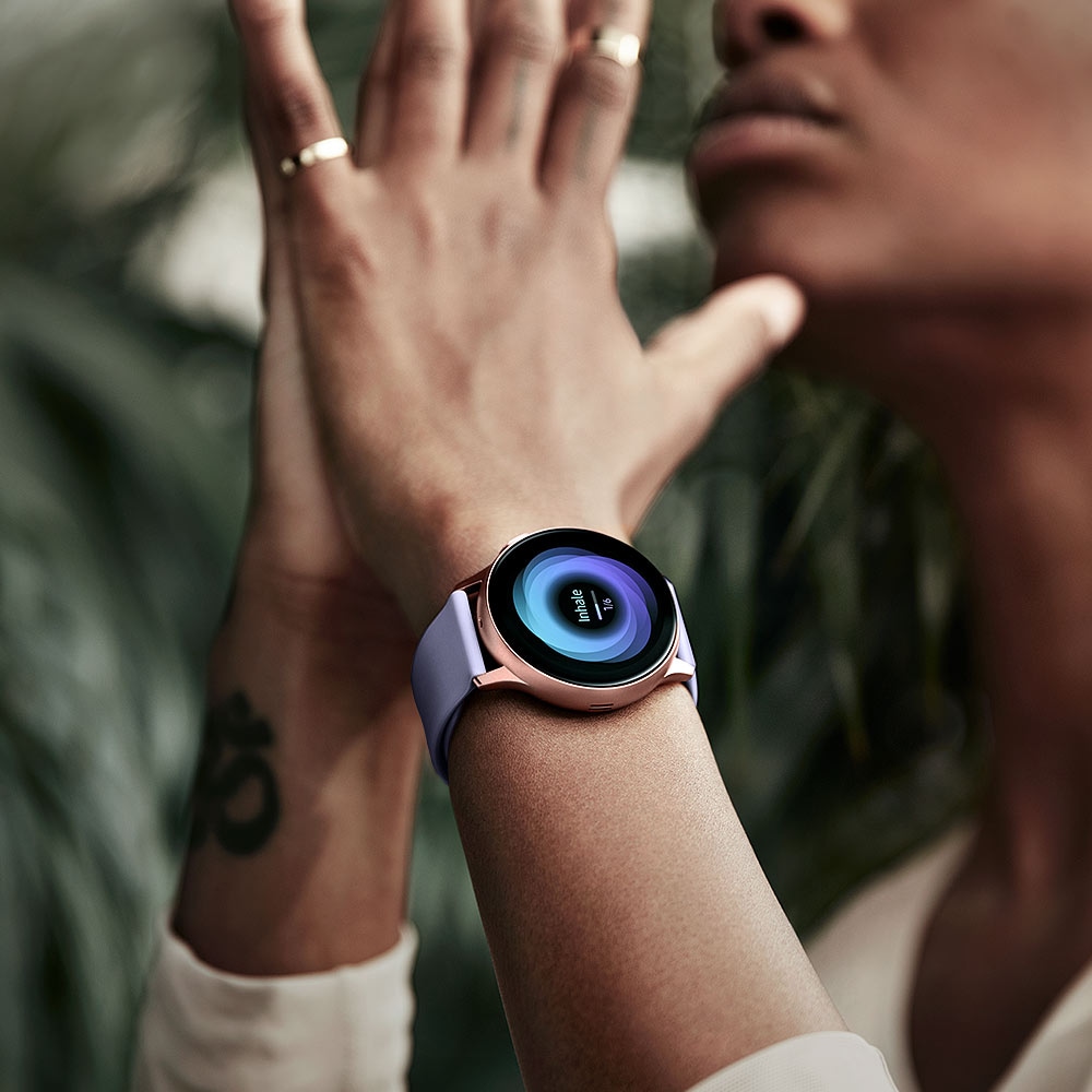 Woman practices yoga with hands in prayer pose while wearing Rose Gold Galaxy Watch Active2. The watch face displays breathing exercises.