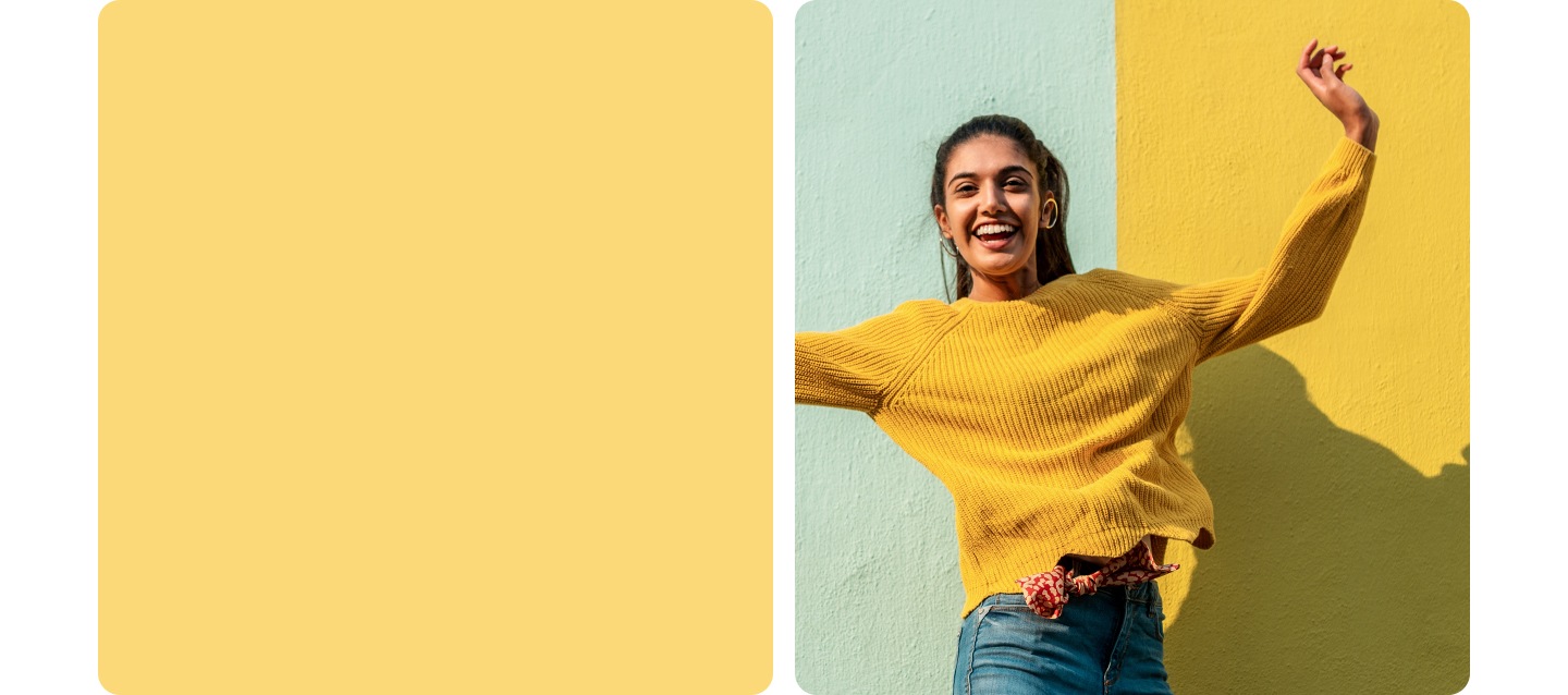 A woman smiling and jumping in front of a two-tone wall. Her yellow sweater matches the yellow of the wall.