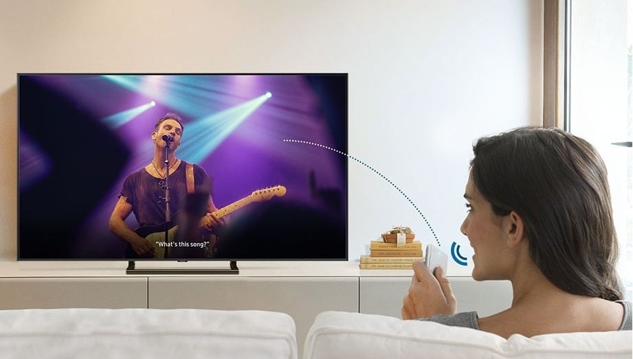 ผู้หญิงคนหนึ่งถามชื่อเพลงที่เล่นอยู่ใน Smart TV จาก Bixby ผ่าน One Remote Control