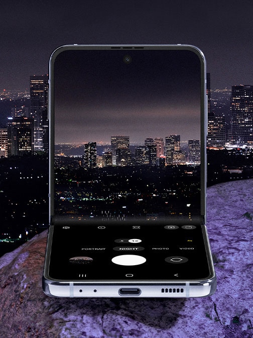 Flex 模式下的 Galaxy Z Flip4。在夜間模式下，內頁螢幕上可以看到相機畫面。這時呈現的是夜間城市天際線的預覽畫面。夜間模式使得城市燈光的色彩和細節變得生動清晰。