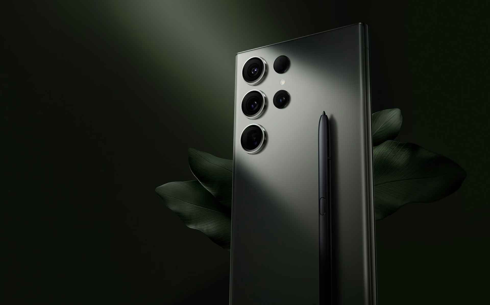 Зелений смартфон Galaxy S23 Ultra (вигляд ззаду) зображено під невеликим кутом. Перед ним лежить перо S Pen.