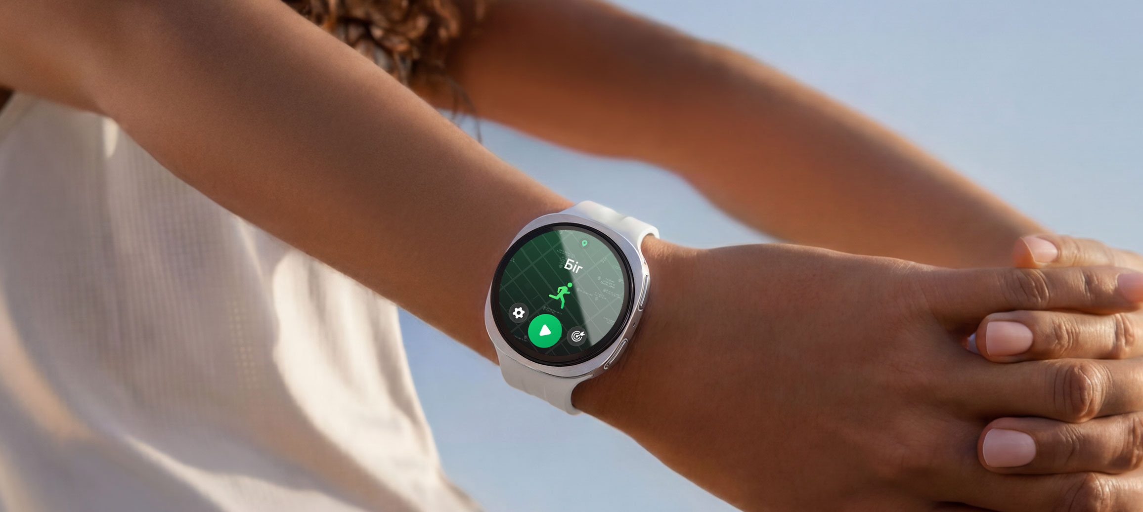 На руці людини Galaxy Watch9 сріблястого кольору зі Спортивним ремінцем бежевого кольору; людина розминає руки, а на дисплеї годинника відкрита програма тренування з бігу, на якій відображається карта маршруту з позначеним місцем.