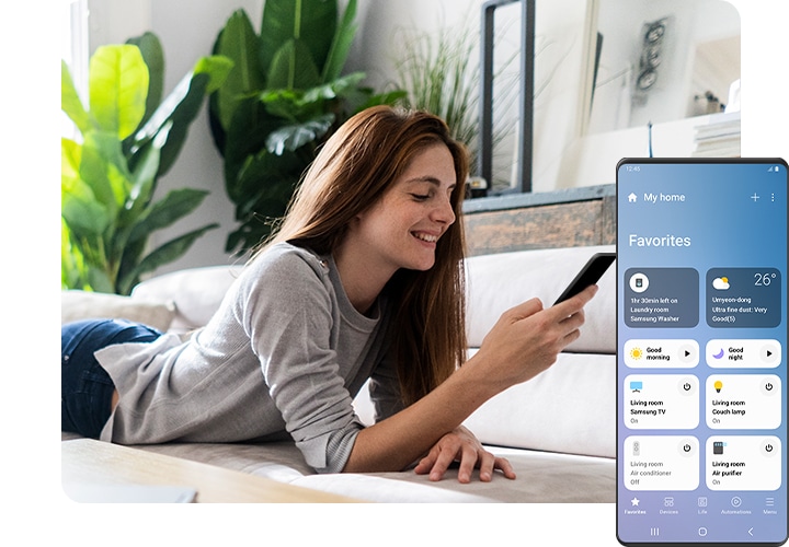A woman is lying on the sofa, smiling and looking at her smartphone. On the right side of foreground, a Galaxy screen shows the SmartThings app GUI with various connected smart home devices, their status, and other routines that could be set, including "Good morning" and "Good night."