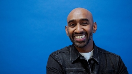 A male in a denim shirt smiles into the camera. 