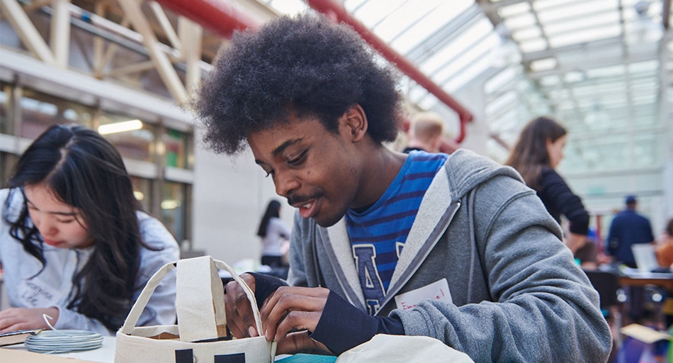 Young man tinkering with his headwear gadget creation in an atrium classroom.