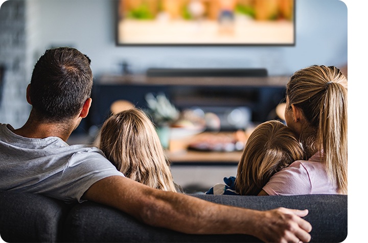 A family sitting on a sofa, watching TV.