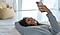 A woman is lying on the floor smiling and looking at Galaxy S25 Ultra with a yellow bean bag visible behind her.
