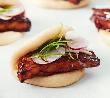 An overhead shot of a bao bun garnished with a radish and chive.