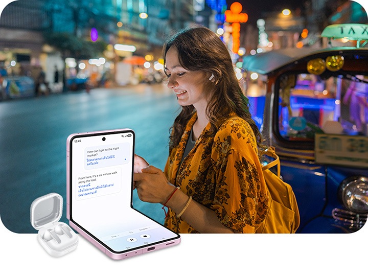 A person is travelling, typing on their smartphone and using Interpreter to communicate in another language. Next, Galaxy Buds4 Pro in White sit in their charging case. Galaxy Z Flip8 in Pink is seen in FlexMode from the main screen and Interpreter is active. Interpreter has translated text into the user's native language.”