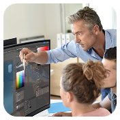 Lifestyle shot of a professional leaning in to help colleagues adjust image values on a Samsung display monitor.
