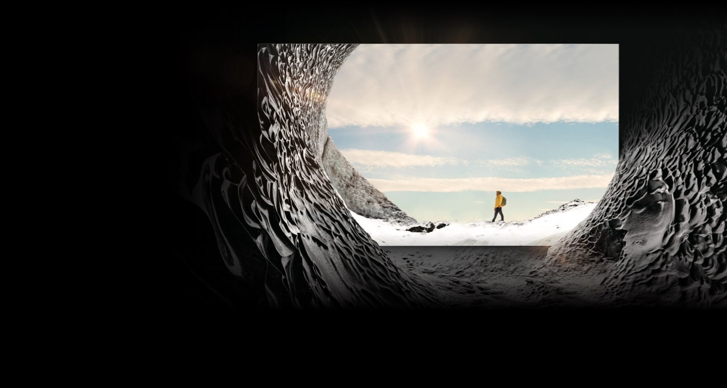 MICRO LED TV is placed inside a mountain cave and is displaying the image of a mountain climber in the sun. The mountain cave blends into the on-screen image to show that the textures of inside and outside the mountain cave are indistinguishable from each other.