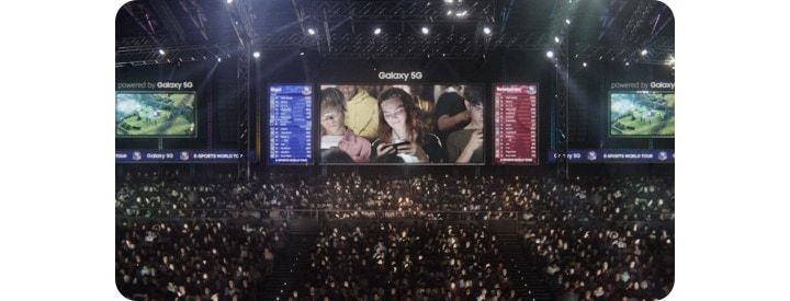 A view of a stadium at an E-sports event, full of people playing on their phones. A Jumbotron screen shows a woman playing on her phone, surrounded by other people doing the same