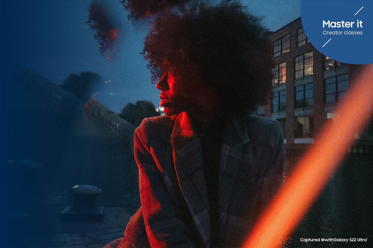 Một người phụ nữ mặc áo khoác nhìn sang trái, được chiếu sáng tinh tế bởi đèn đỏ phía trước bầu trời xanh. Lớp học Master it Creator được chụp #withGalaxy S22 Ultra1