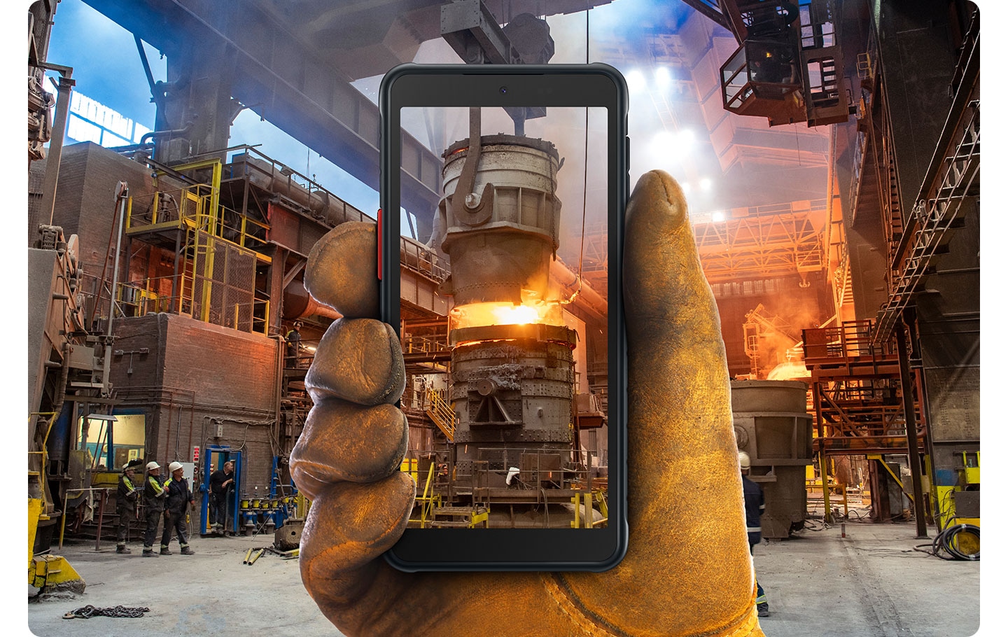 Eine Hand mit gelben Schutzhandschuhen hält das Galaxy XCover 5, auf dessen Display ein Hochofen im Hintergrund der Fabrik zu sehen ist.