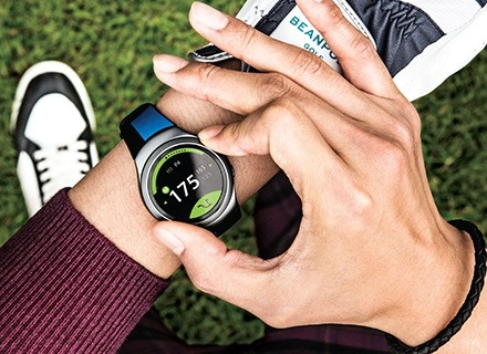 An image of a man turning the dark gray Gear S2's rotating bezel to check out S Health-related information.  