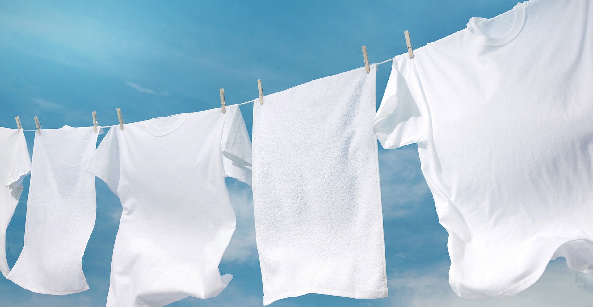Lint-free white towels and t-shirts are hanging out to dry on a clothes line outside.