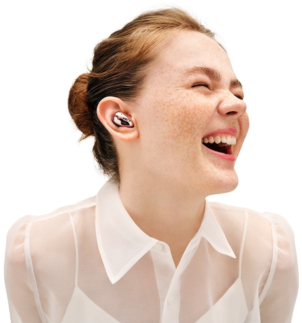 Front view of Galaxy Buds Live in Mystic Bronze. Right Galaxy Buds Live earbud disappears as the left earbud shrinks and fits in the ear of a woman laughing.