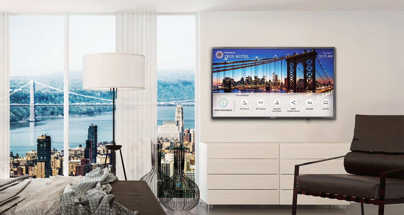 An image showing a Samsung hospitality TV installed on the wall in a hotel room with a bed and a chair. The TV screen displays the hotel information page.